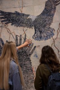 Photograph of two young women looking at a tapestry by Kiki Smith of two large eagles flying in the exhibition I am a Wanderer at Modern Art Oxford