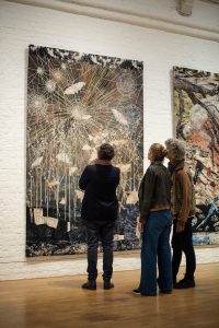 Three figures facing a tapestry by Kiki Smith depicting large spider webs and moths in shades of blue and brown in the exhibition I am a Wanderer at Modern Art Oxford